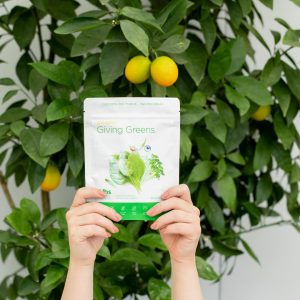 Giving Greens Slenderiiz product held up by hands with lemon tree in background